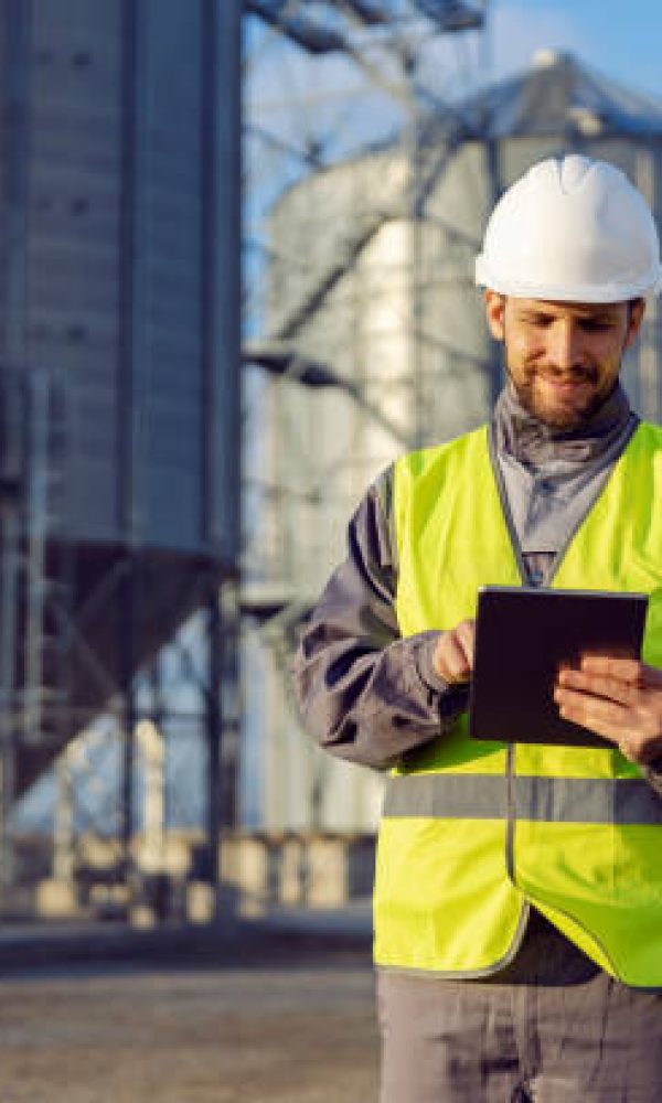 A supplies worker uses a tablet in front of the silos.